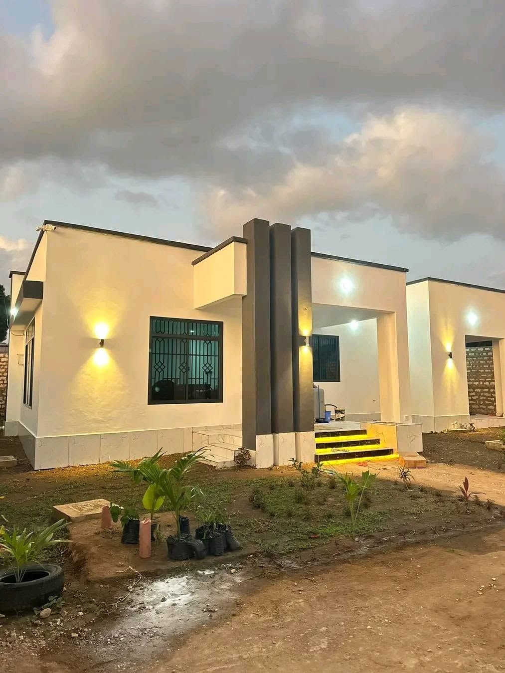 Single-storey white house with wall lights on at dusk.