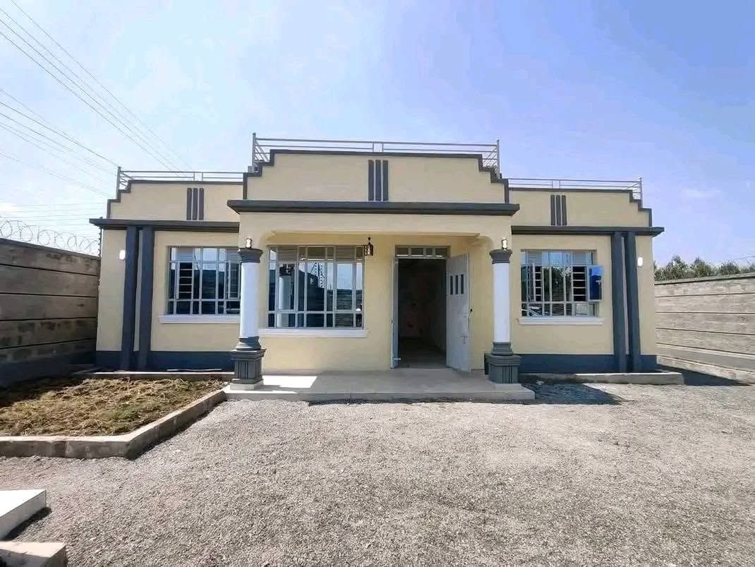 Single-storey cream house with a parapet roof and columned porch, gravel yard.