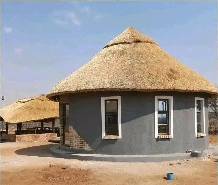 Round house with grey walls, white window frames and a thatched roof.