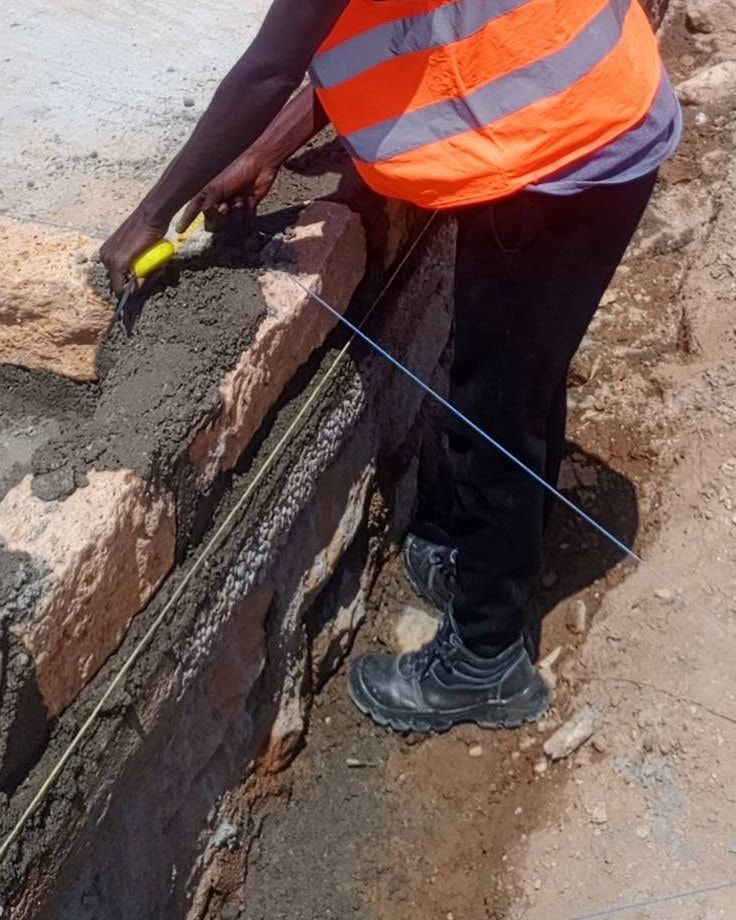 A tape measure and a blue string line held along a new stone foundation course.