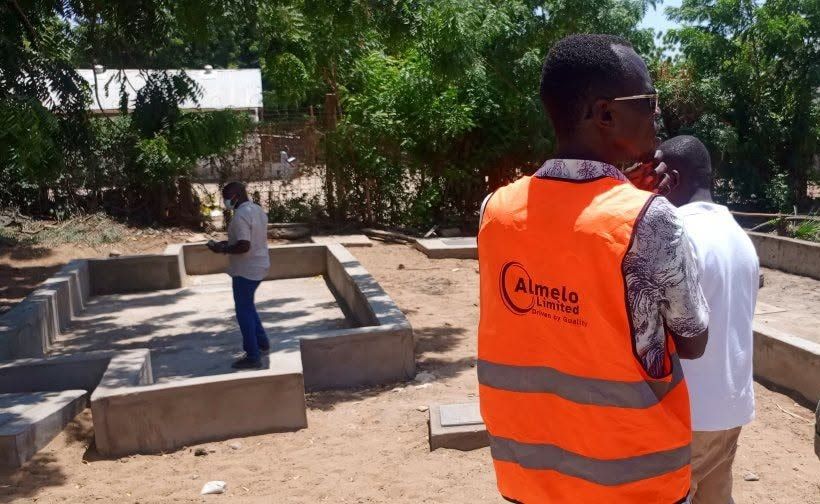 An Almelo engineer in an orange "Almelo Limited, Driven by Quality" vest beside new septic chambers in Lodwar.