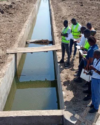 Engineers checking papers beside a plank footbridge over the Napak canal.
