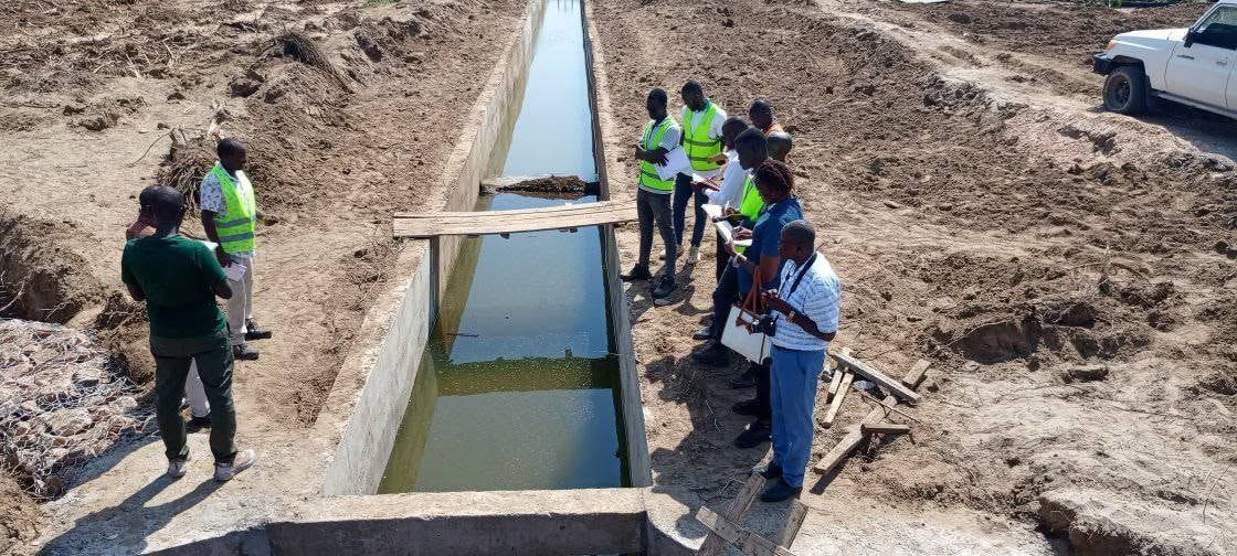 Engineers checking papers beside a plank footbridge over the Napak canal.