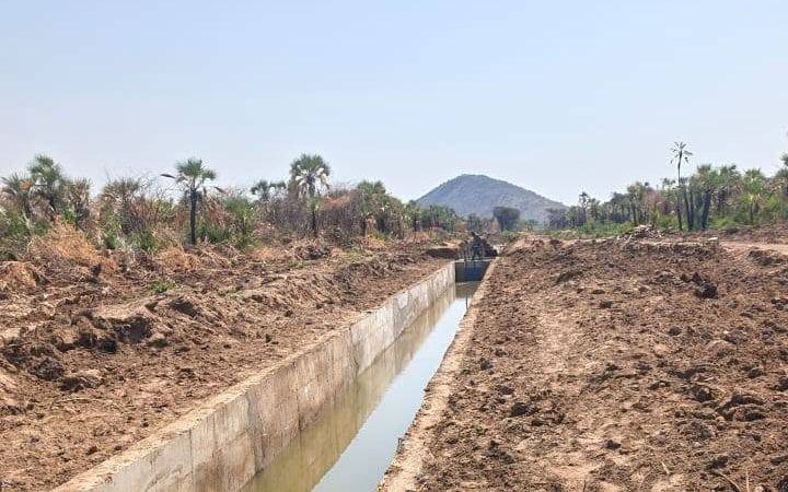 A straight concrete-lined irrigation canal at Napak, full of water, running towards a lone hill under a clear sky.