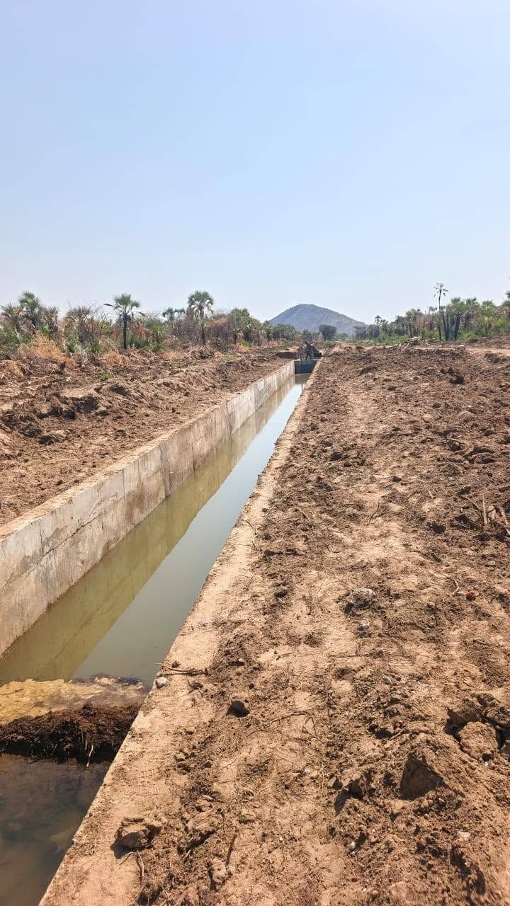 A straight concrete-lined irrigation canal at Napak, full of water, running towards a lone hill under a clear sky.