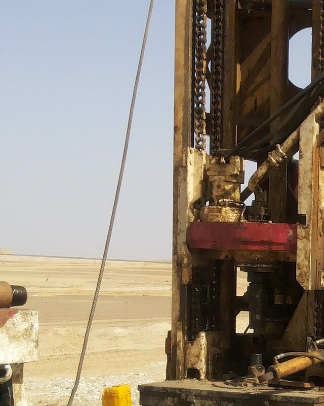 The mast of a drilling rig standing on dry, open ground.